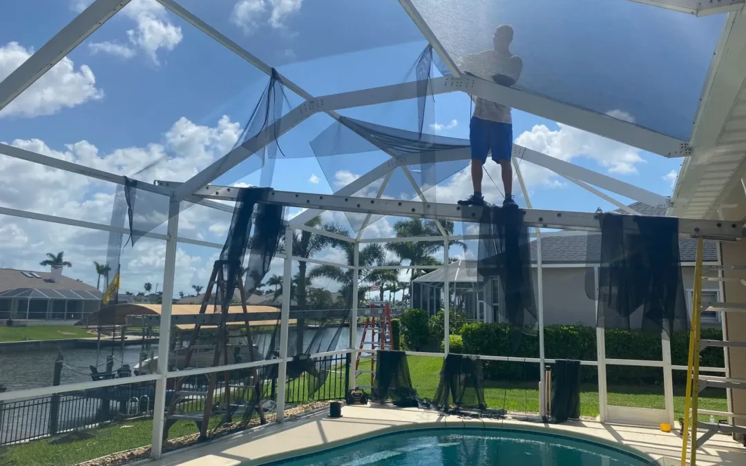 A man is standing on top of a screened in pool.